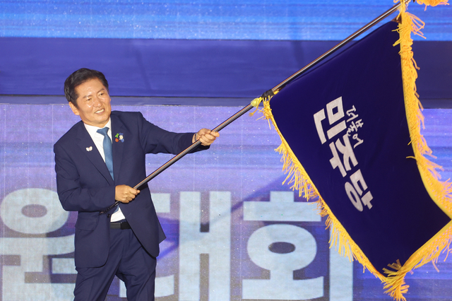 정청래 신임 더불어민주당 대표가 2일 경기도 고양시 킨텍스에서 열린 전국당원대회에서 김병기 당대표 직무대행 겸 원내대표로부터 받은 당기를 흔들고 있다. [연합뉴스]