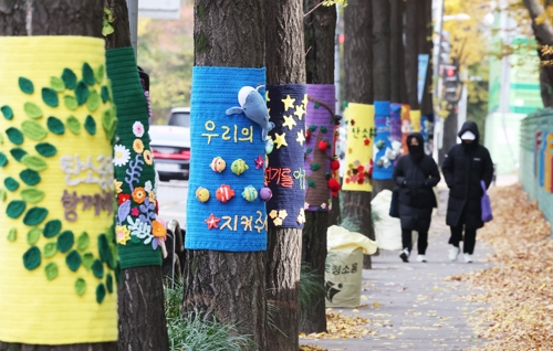 북쪽에서 찬 공기가 유입되며 추위가 찾아온 17일 경기도 광명시의 한 거리에서 두꺼운 옷차림의 시민들이 뜨개옷 입은 가로수길을 걷고 있다. [광명=연합뉴스]