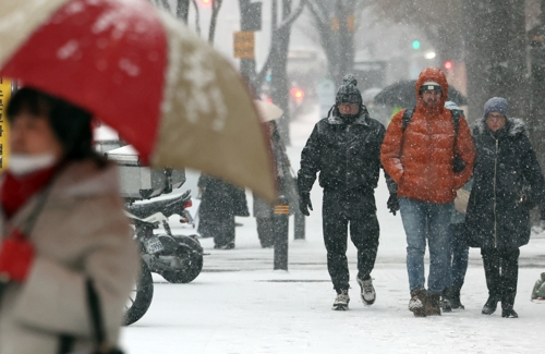 12일 서울 종로구 종각역 인근에서 시민들이 눈을 맞으며 이동하고 있다. [연합뉴스]