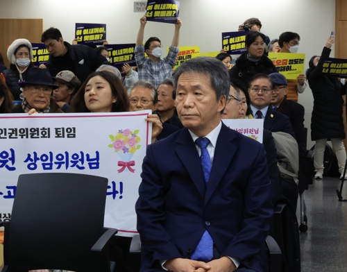 지난 5일 서울 중구 국가인권위원회에서 열린 김용원 상임위원 이임식에 김 위원이 참석해 행사시작을 기다리고 있다. 연단 뒤편에서 전국공무원노동조합 인권위 지부 조합원들이 공식회의록에 기록된 김 위원의 폭언 발언을 손팻말에 적어 시위하고 있다. [연합뉴스]