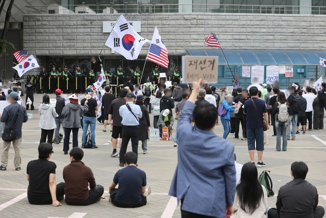 6·3 지방선거 투표용지 부족 사태를 규탄하며 재선거를 요구하는 ‘잠실 개표소 봉쇄 시위’가 계속되고 있는 8일 서울 송파구 올림픽공원 핸드볼경기장 출입구 앞에서 참가자들이 구호를 외치고 있다. [연합뉴스]