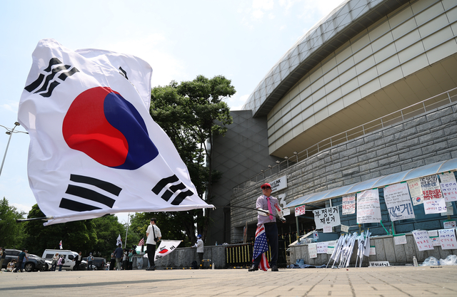 6·3 지방선거 투표용지 부족 사태를 규탄하며 재선거를 요구하는 ‘잠실 개표소 봉쇄 시위’가 계속되고 있는 9일 서울 송파구 올림픽공원 핸드볼경기장에서 한 참가자가 태극기를 흔들고 있다. [연합뉴스]