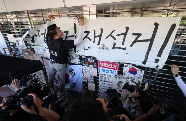 6·3 지방선거 투표용지 부족 사태로 촉발된 잠실 개표소 봉쇄 시위가 이어진 8일 서울 송파구 올림픽공원 핸드볼경기장에서 경찰이 ‘부정선거 재선거’라는 문구가 적힌 종이를 제거하고 있다.  [연합뉴스]
