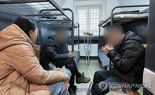 우크라이나군에 생포된 북한군 포로 백모씨와 리모씨가 28일(현지시간) 우크라이나 내 포로수용소에서 김영미PD와 접견하며 탈북민단체들이 보낸 북한음식 ‘두부밥’을 먹고 있다. 침대(왼쪽 상단)에 이들이 직접 그린 김정은 북한 국무위원장의 초상화가 붙어 있다.   [겨레얼통일연대 제공=연합뉴스]